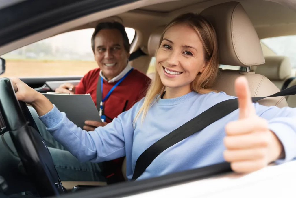 Learner driver smiling and giving thumbs up during a lesson with instructor, showing confidence while learning how many driving lessons do you need.